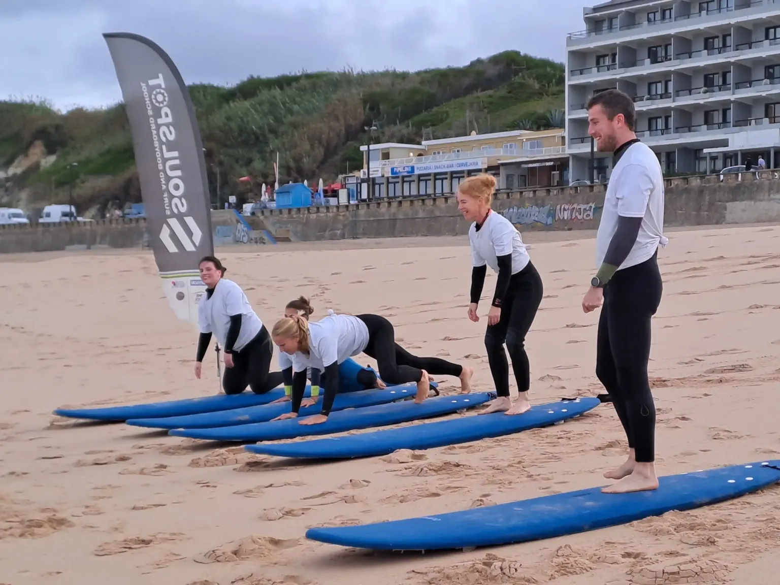 Surf students lying on boards on the beach with an instructor standing beside them