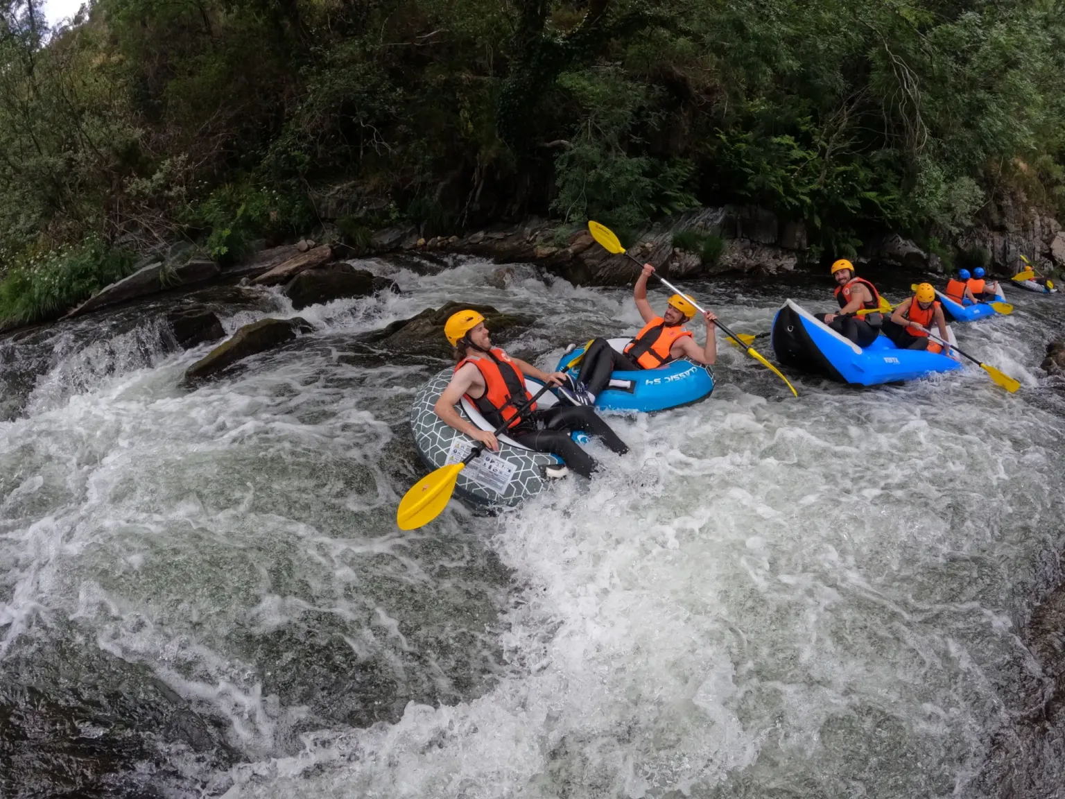 Paddlers in inflatable boats running rapids in a forested gorge