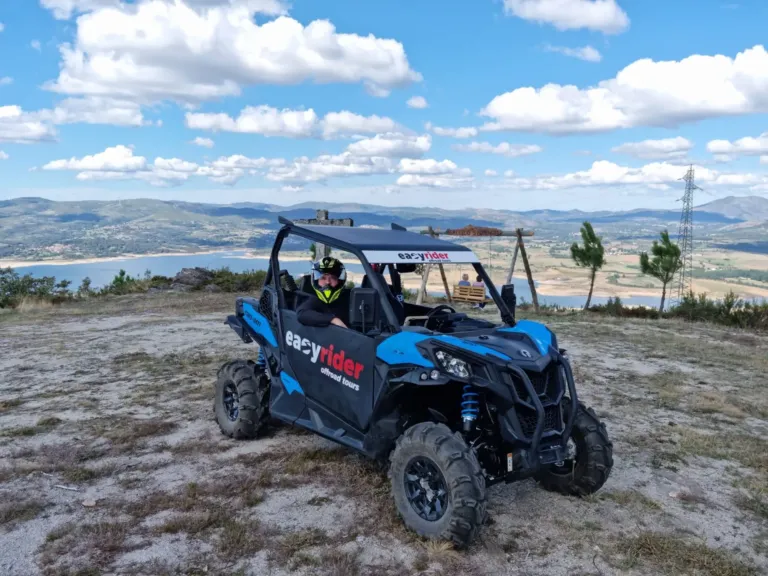 Blue buggy parked on a hilltop with a reservoir and mountains behind