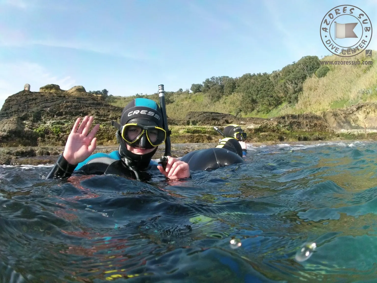 Snorkeller in a mask waving at the surface beside a rocky shore