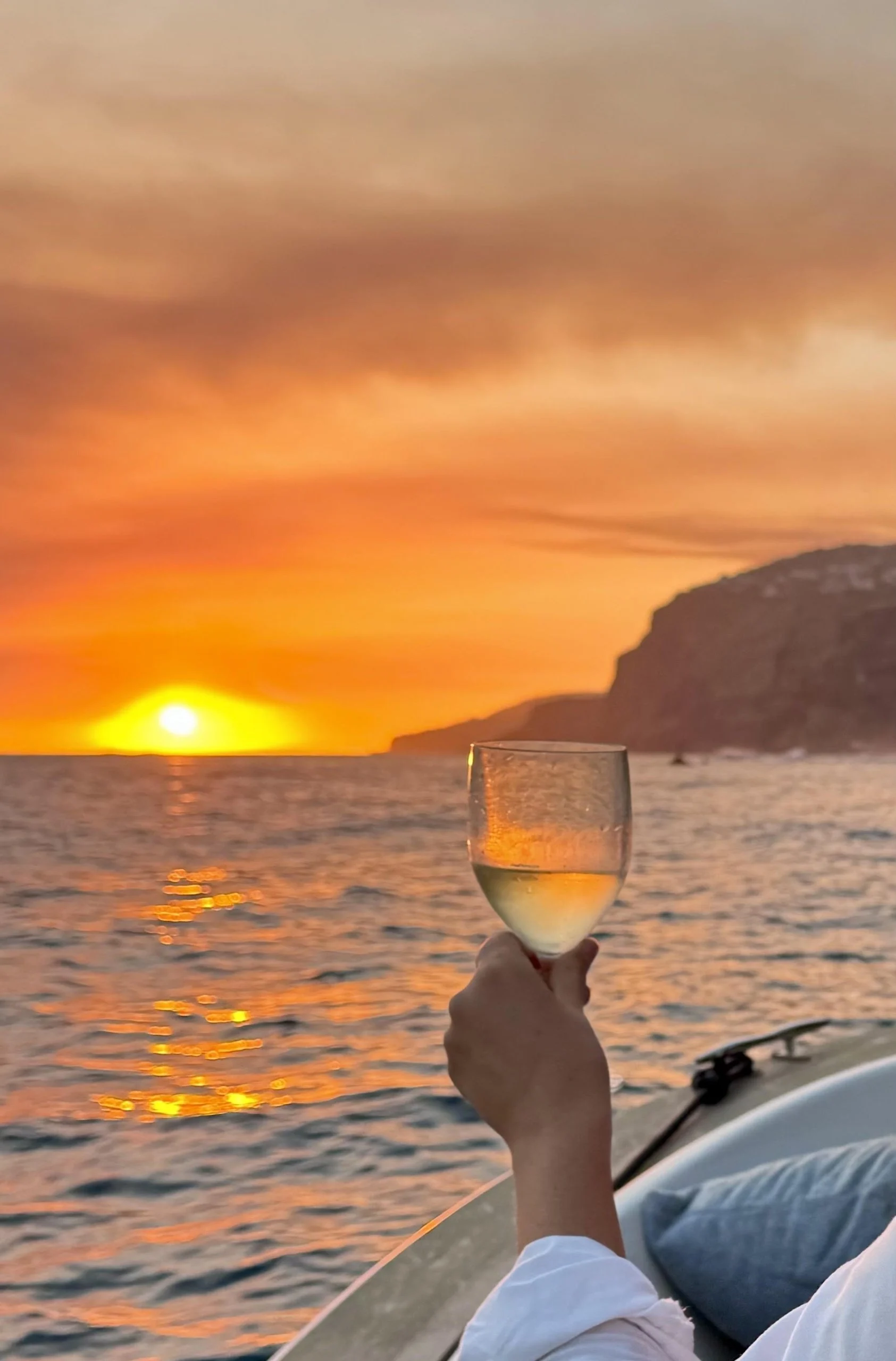 Hand holding a glass of white wine against a sunset over the sea