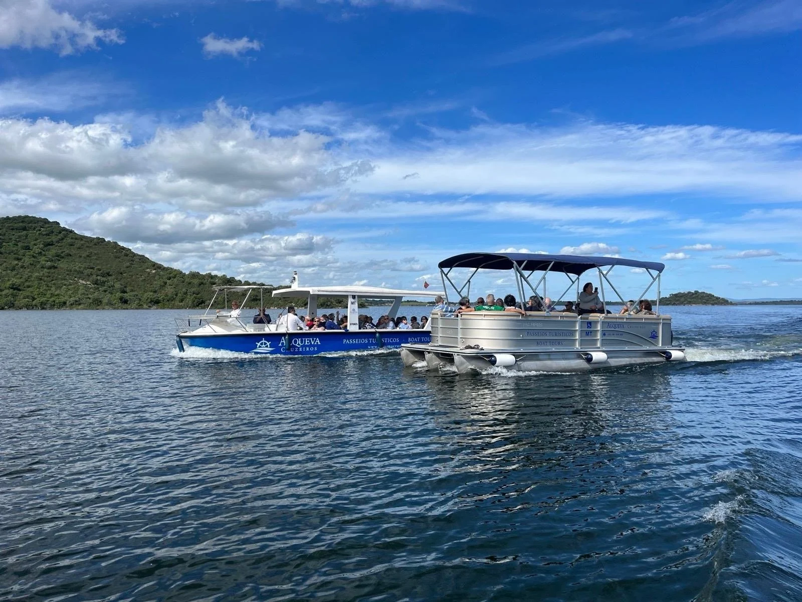 Two passenger pontoon boats on a lake beneath blue skies