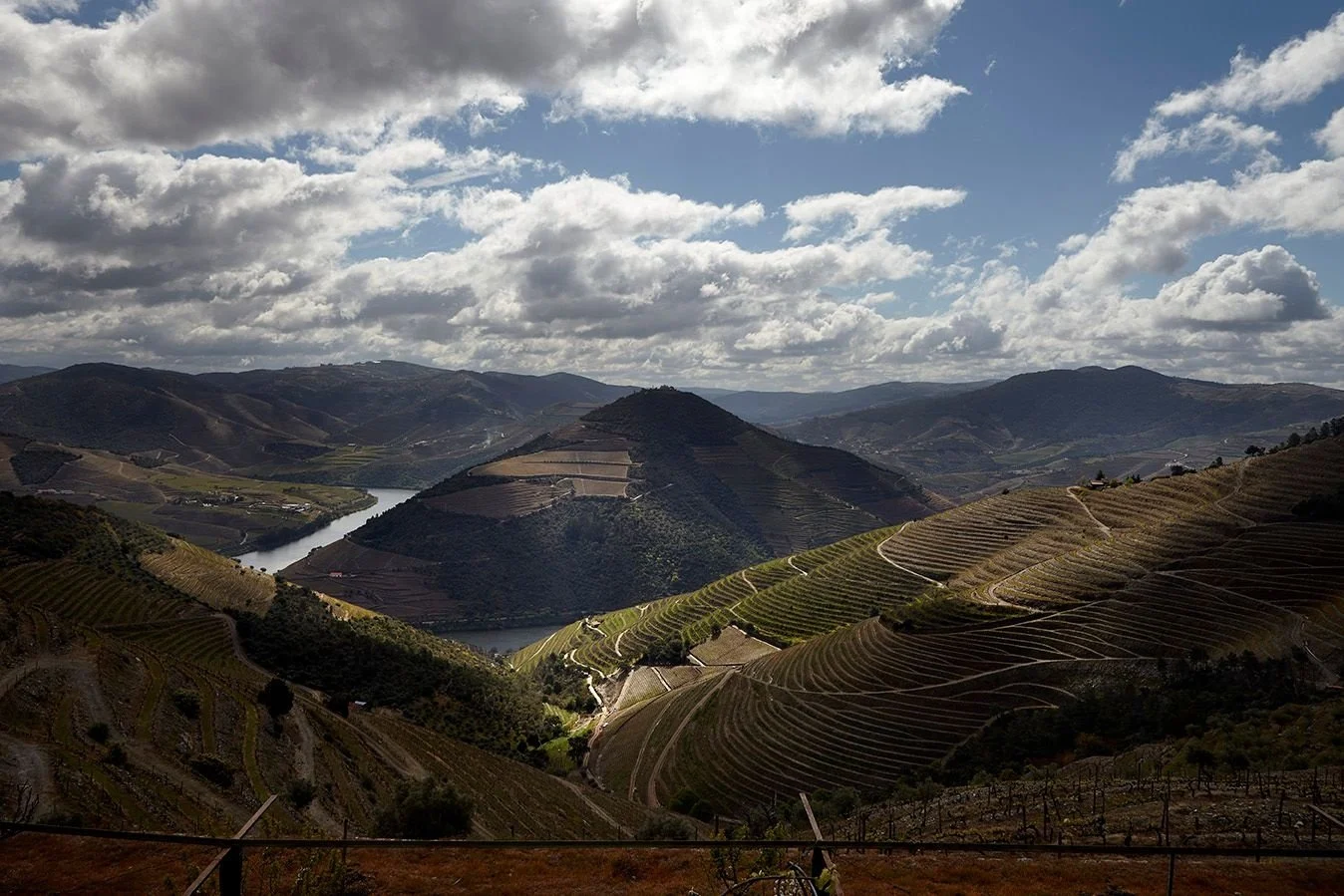 Terraced Douro hills with a river bend under dramatic clouds