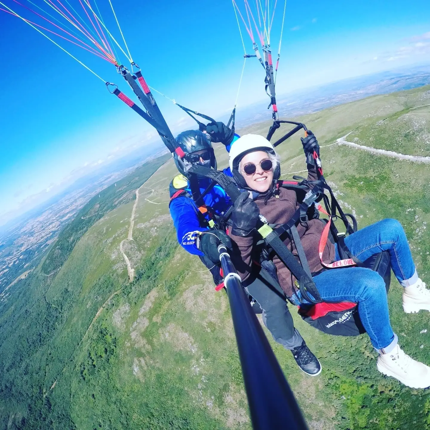 Tandem paraglider flying over green hills