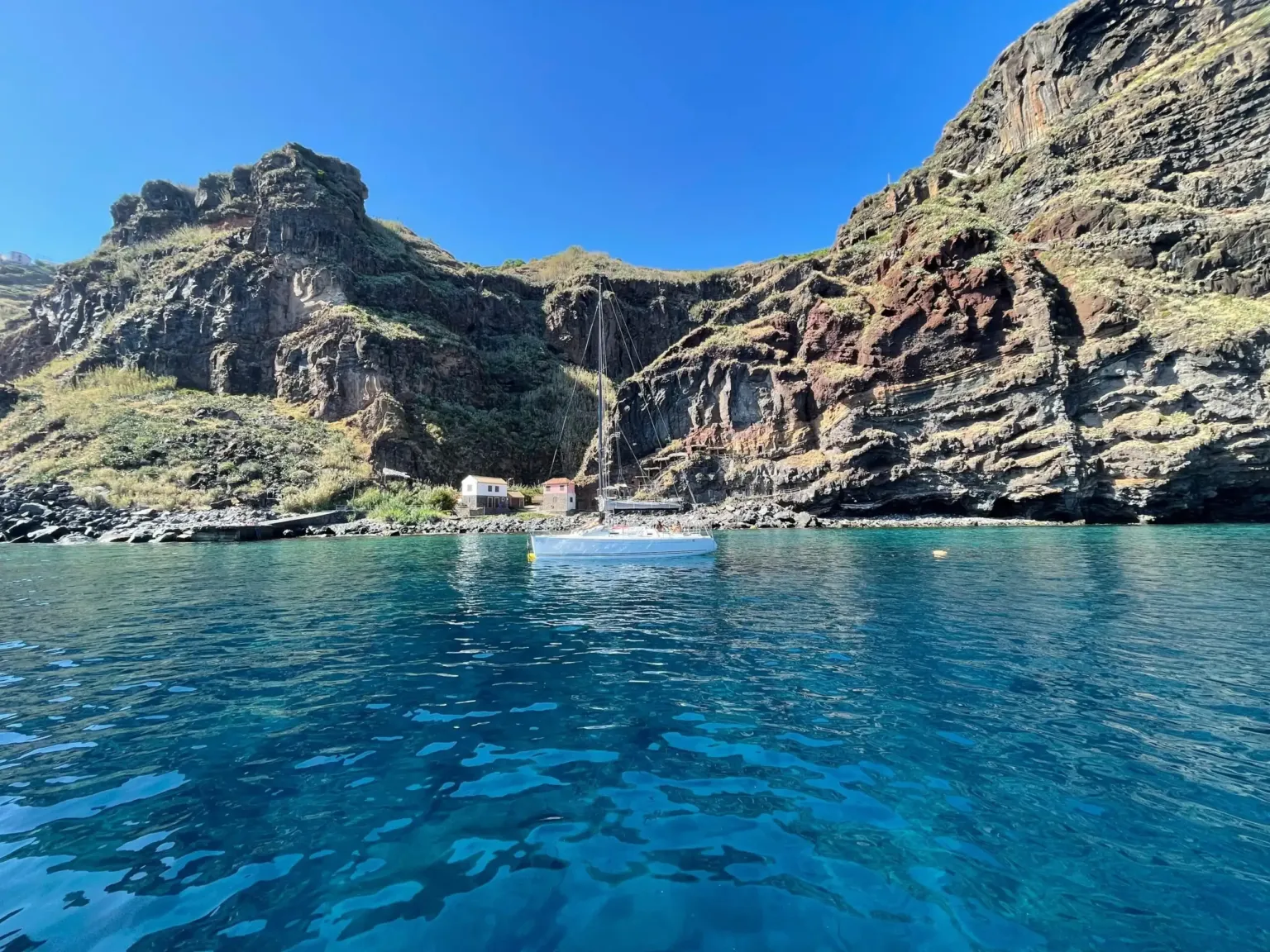Sailing boat at anchor in a bay below steep rust-red cliffs