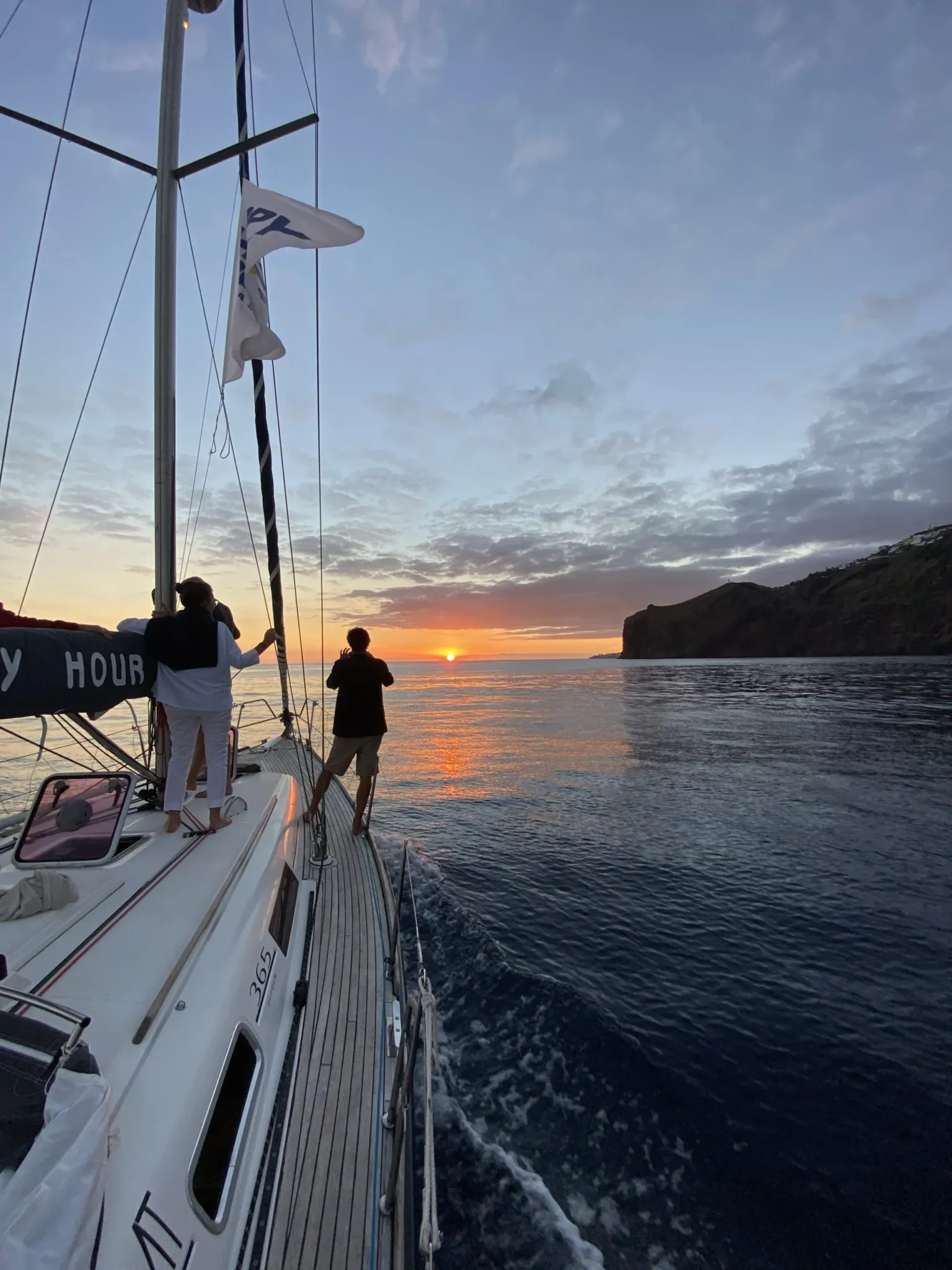 Two people at the bow of a sailboat watching the sun set