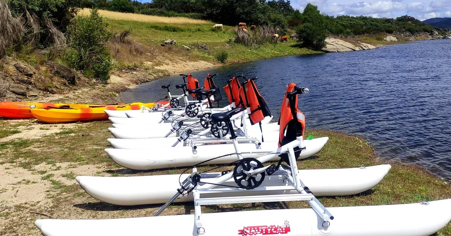 White water bikes lined up on a lakeshore beside kayaks