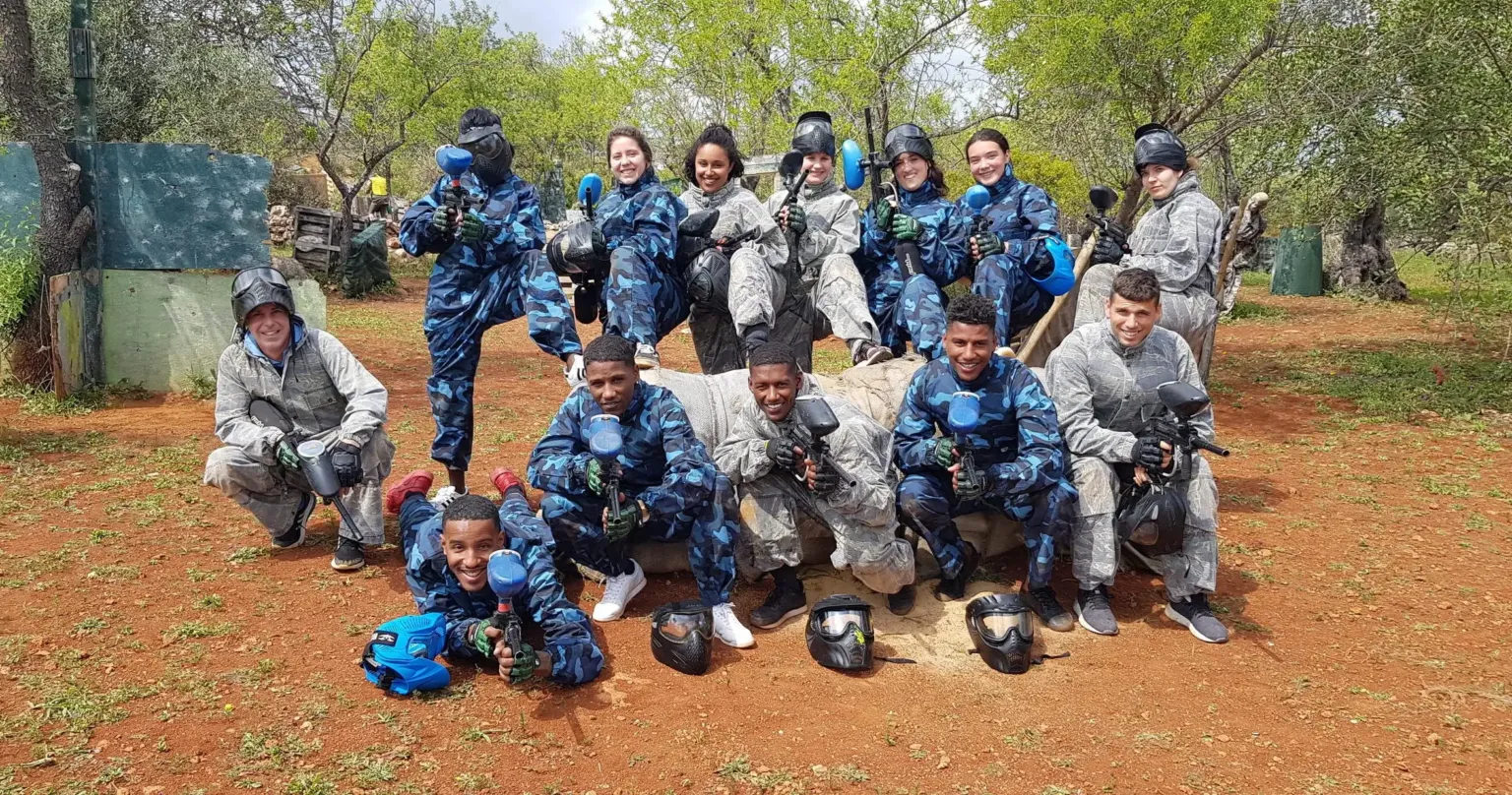 Group in blue camouflage gear and masks posing at a paintball field