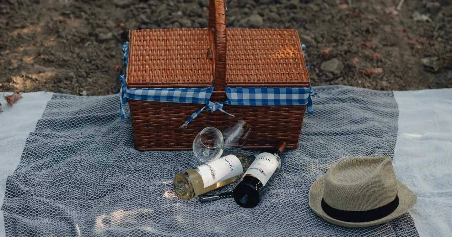 Wicker picnic basket with a hat and wine bottles on a blanket