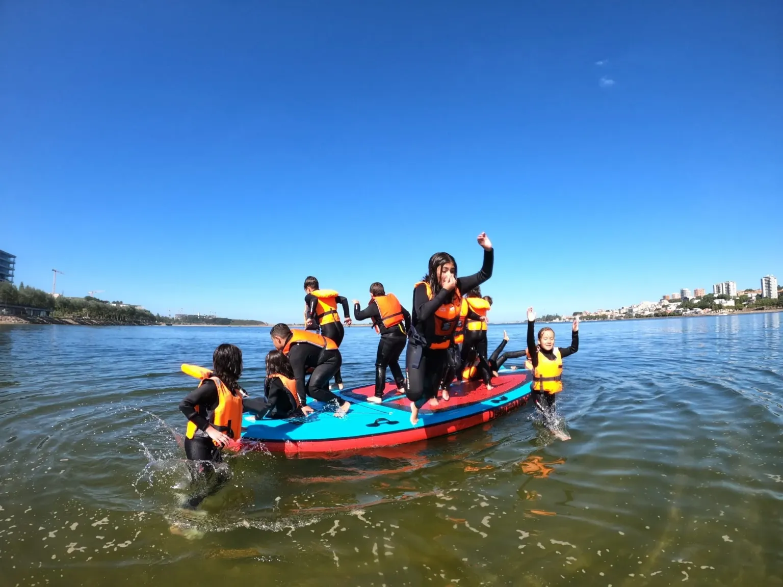 Children in life jackets cheering on a large inflatable board on the water