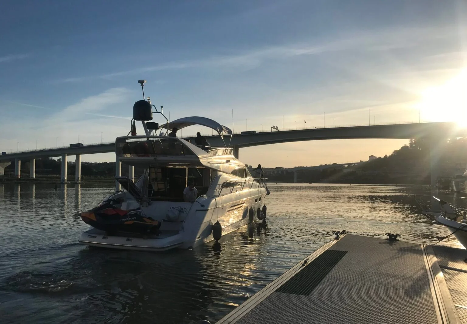 Motor yacht moored at a pontoon with a bridge and low sun behind