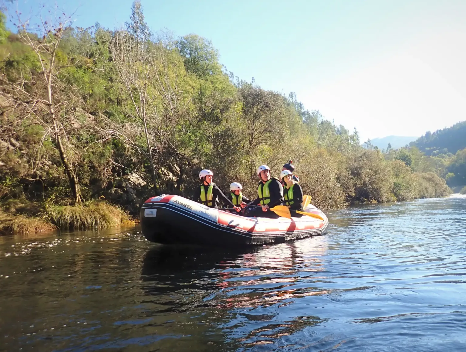 Raft with paddlers on a quiet river between wooded banks