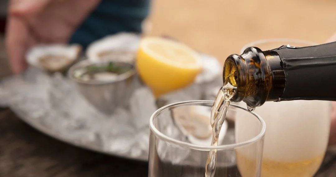 Sparkling wine being poured beside oysters and a lemon on ice