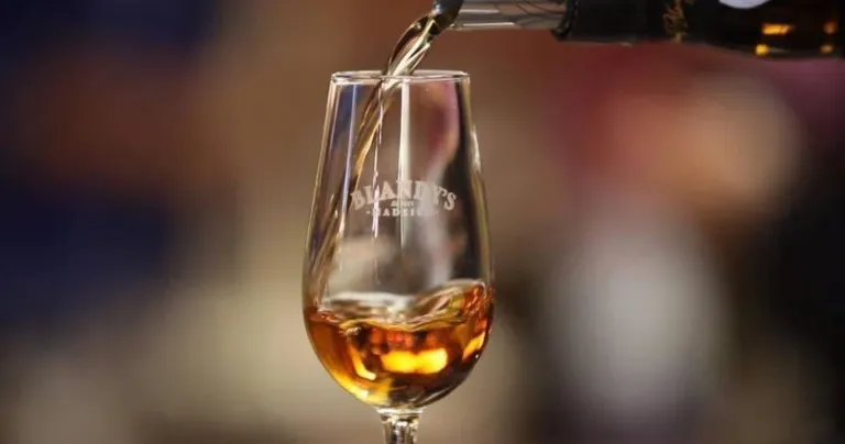 Amber fortified wine being poured into a branded tasting glass
