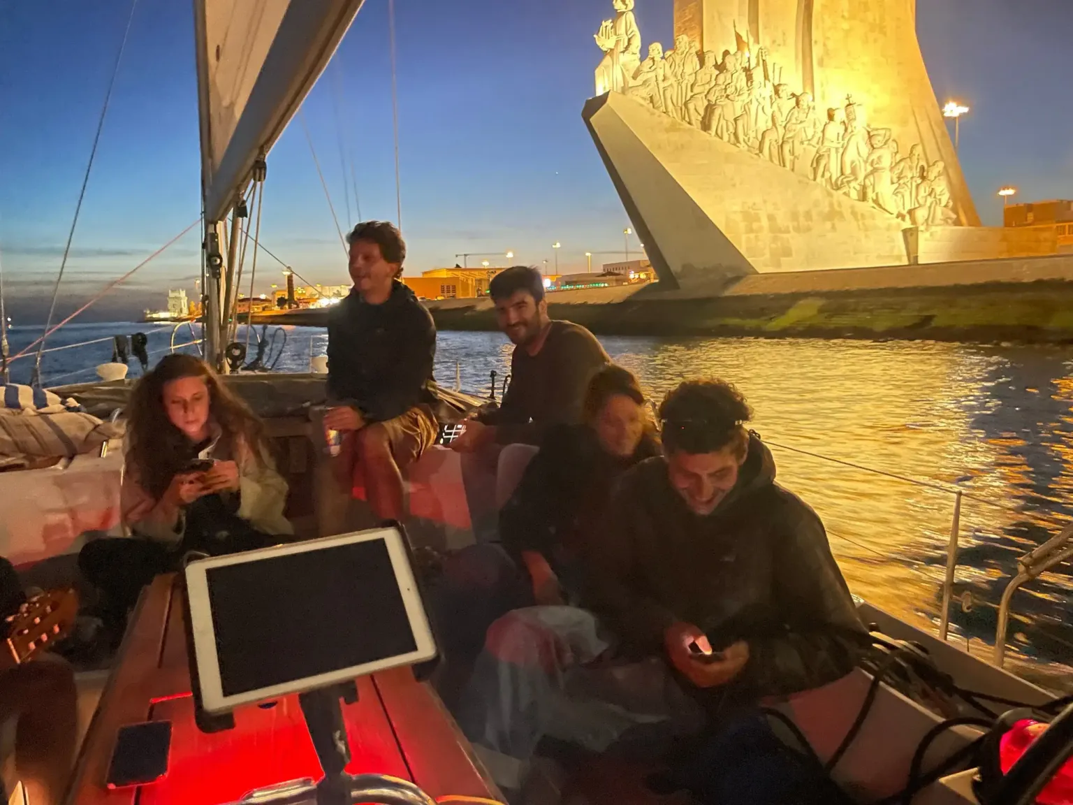 Vrienden op een zeilboot ’s nachts met een verlicht monument op de achtergrond