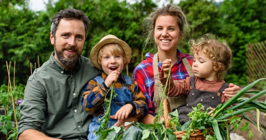 Smiling family with two children holding freshly picked vegetables outdoors