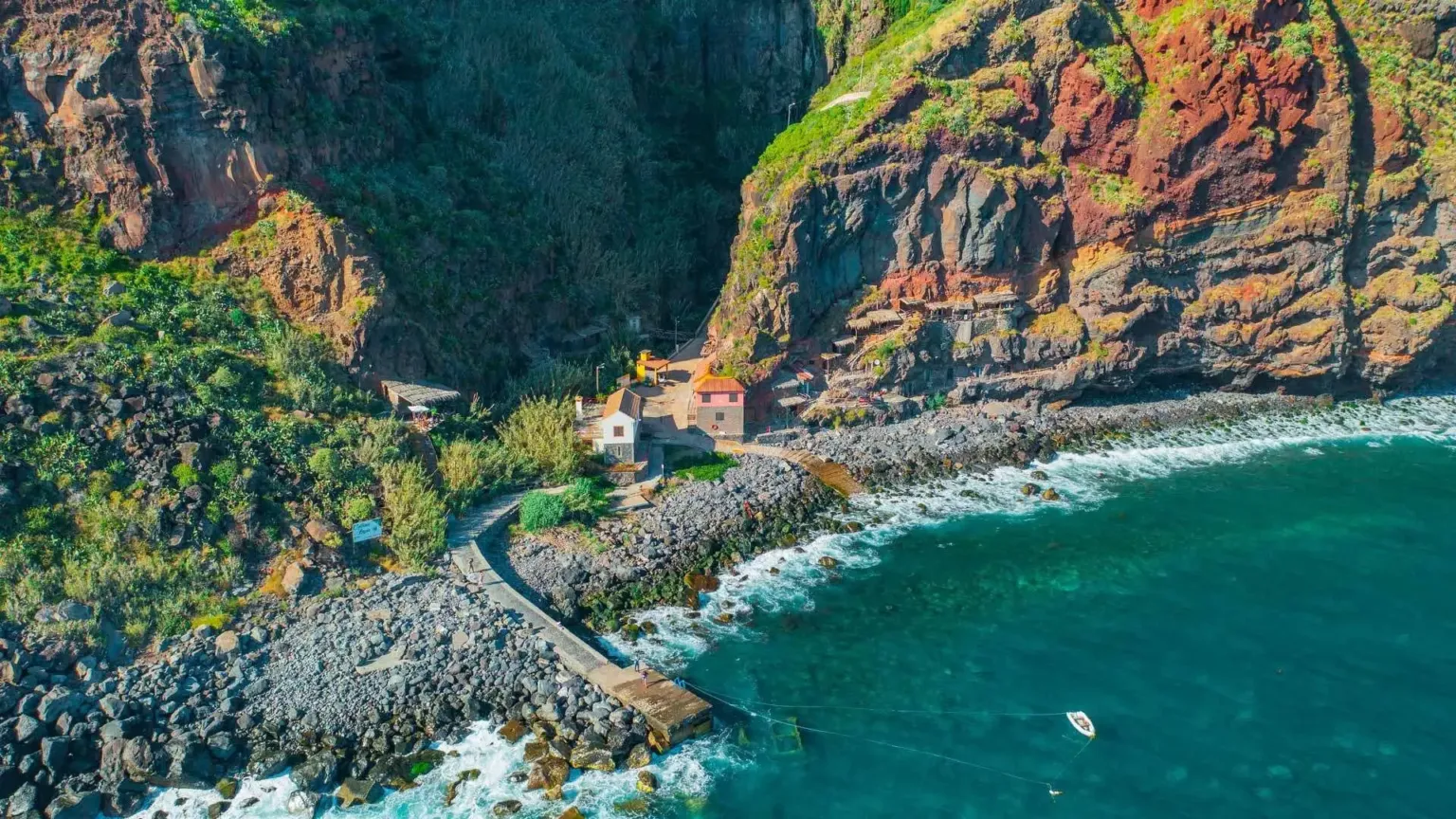 Aerial view of a seaside hamlet beneath steep red-green cliffs