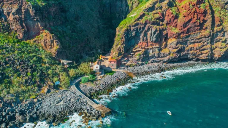 Aerial view of a seaside hamlet beneath steep red-green cliffs