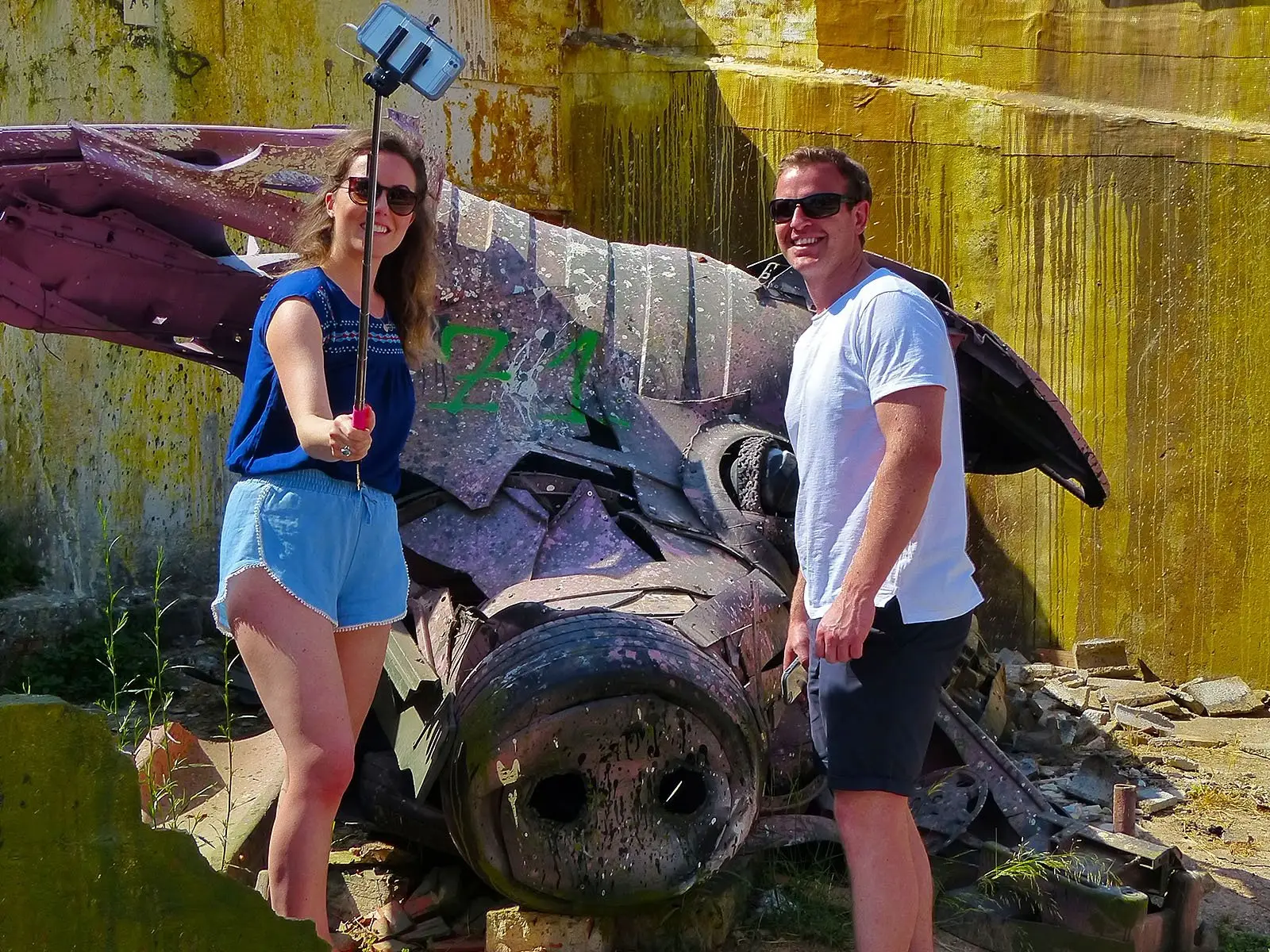 Couple taking a selfie in front of a graffiti-covered wreck