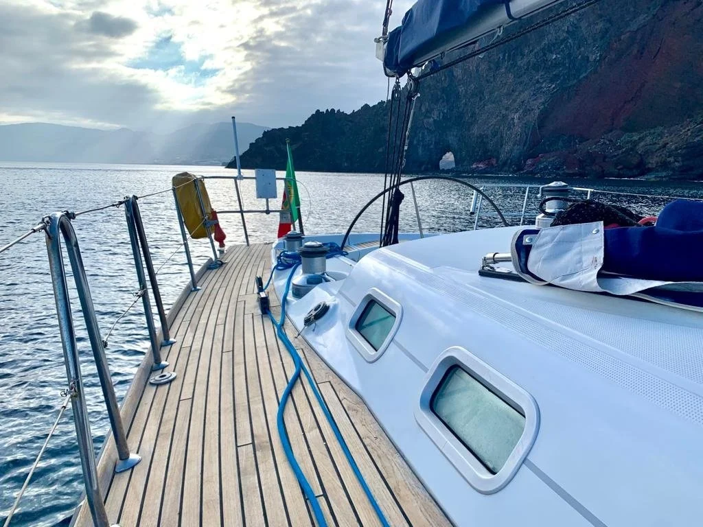 Teak deck of a sailing yacht beside a dark rocky coast