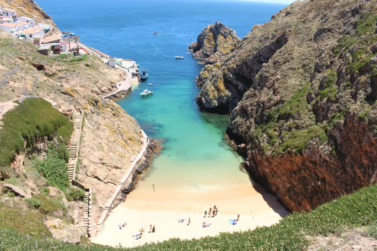 Small sandy cove between steep rocky cliffs with a walled path