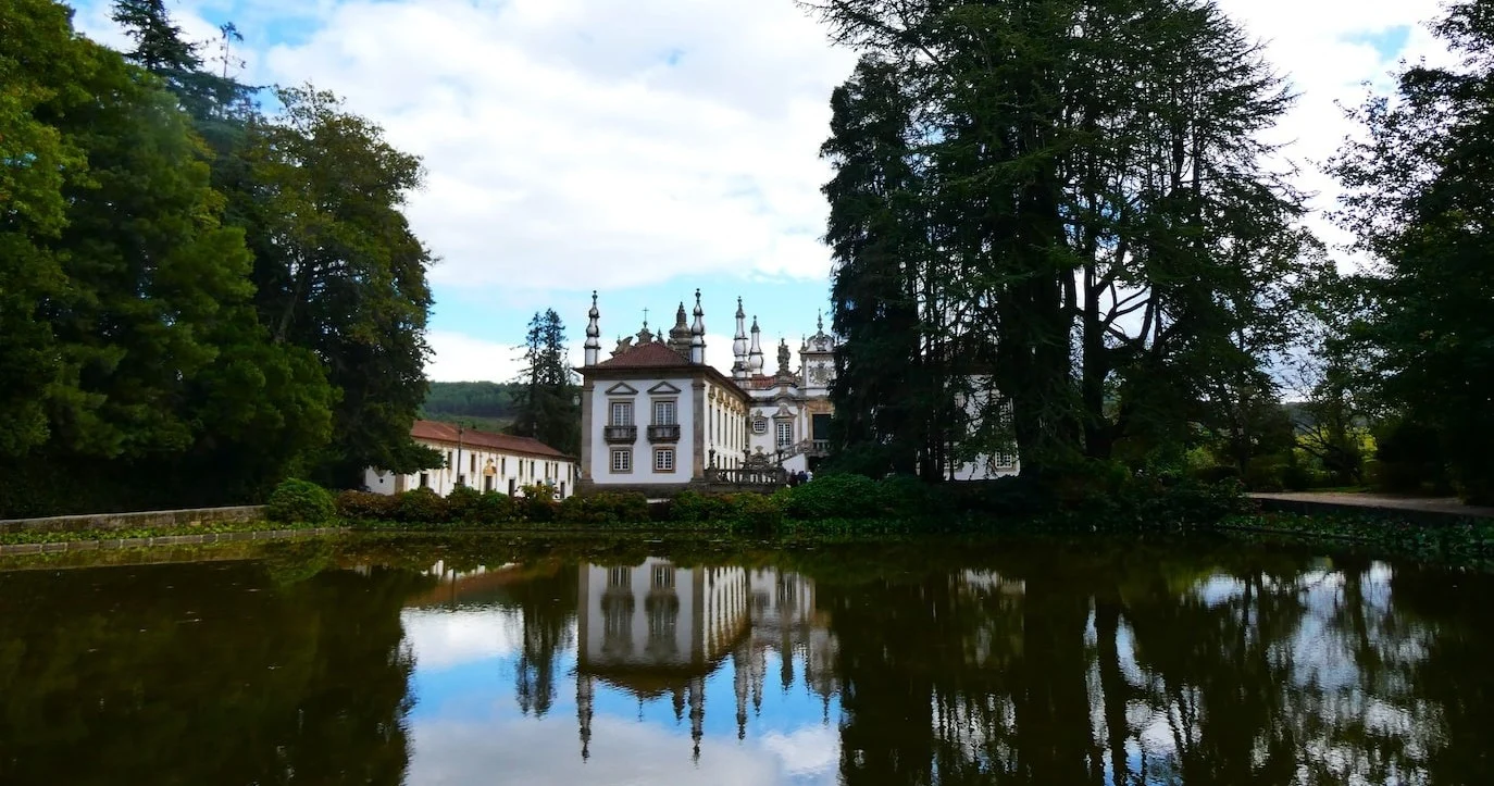 Manor house reflected in a still pond among tall trees