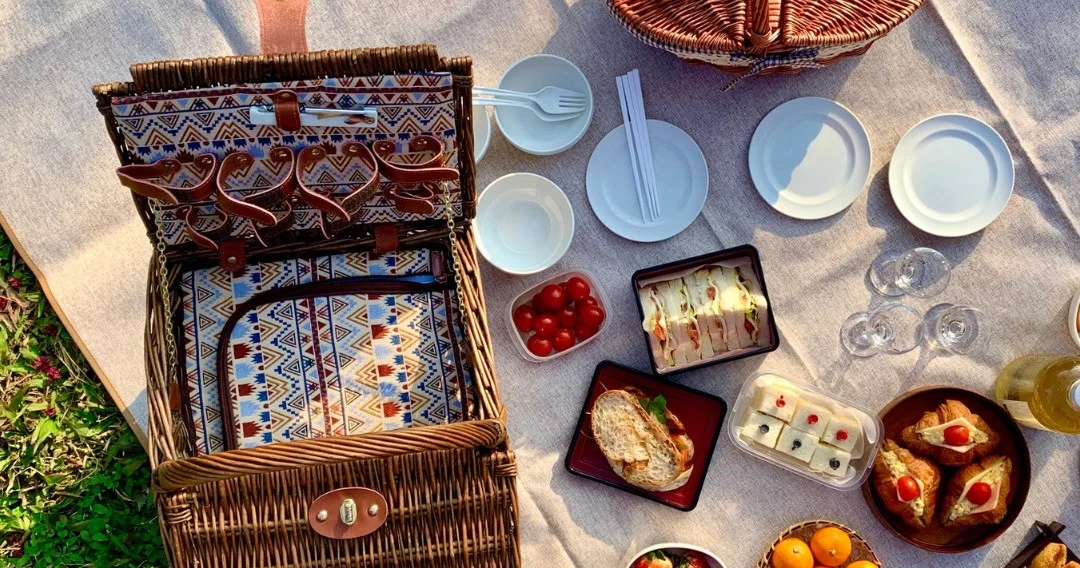 Picnic basket, plates and snacks spread on a blanket