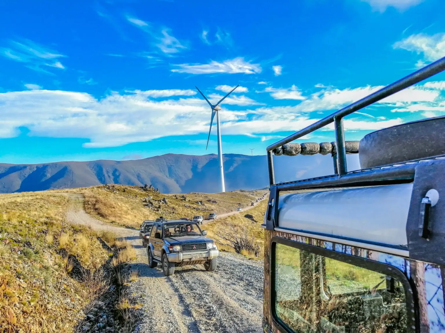 Jeep driving along a gravel mountain road with a wind turbine on the ridge