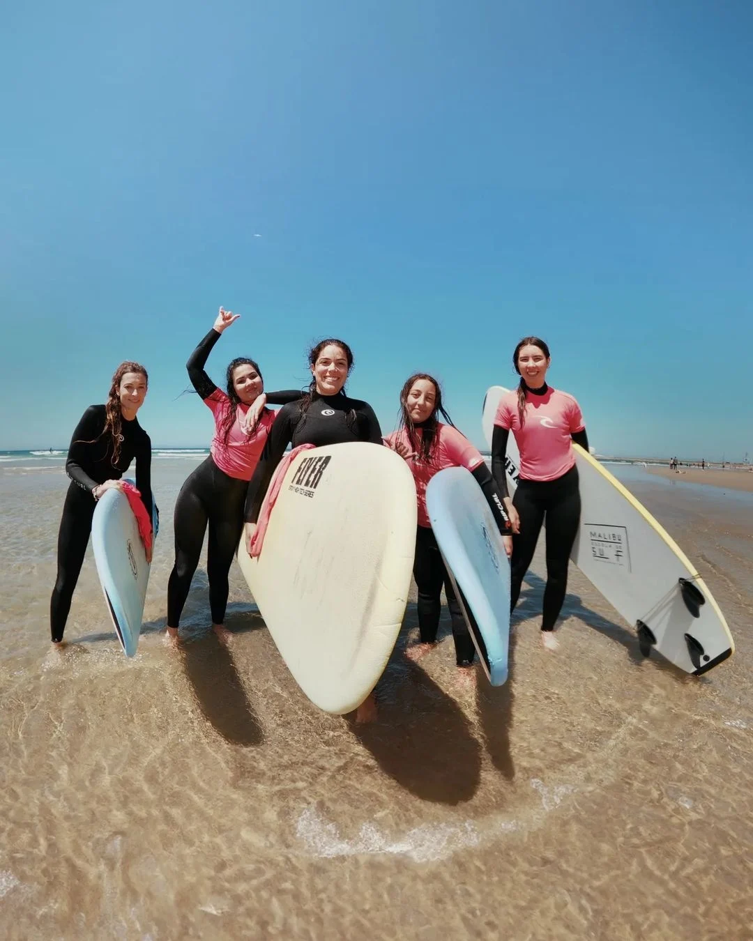 Group of smiling women in wetsuits with surfboards on a beach
