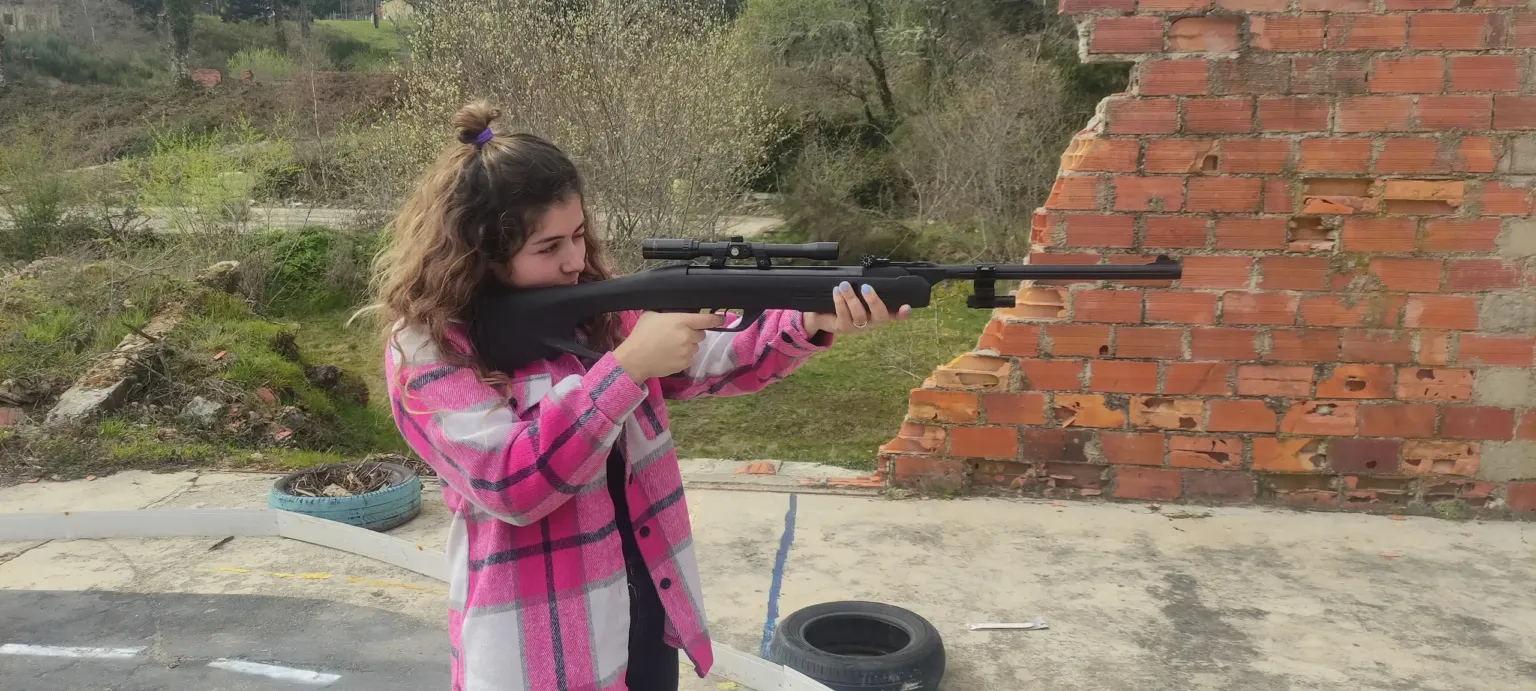 Girl aiming an air rifle at a target beside a brick wall