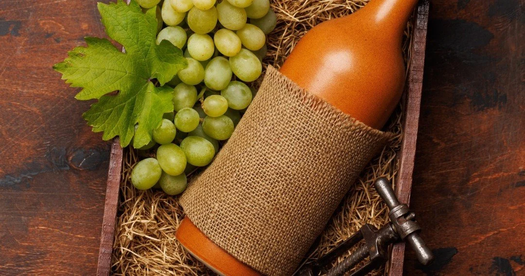 Terracotta wine bottle and green grapes on a wooden tray