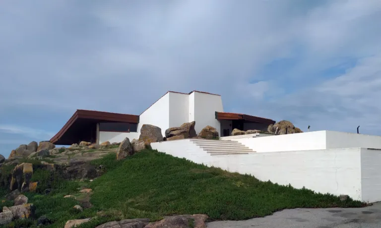 Low white modern building with an overhanging dark roof on a rocky slope
