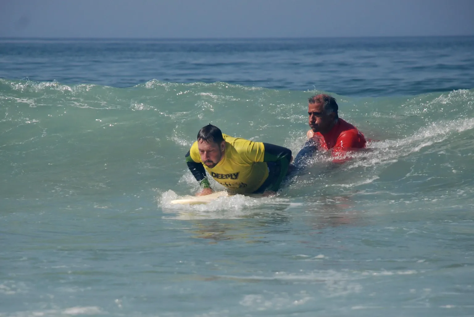 Instructor and student paddling a surfboard into a wave