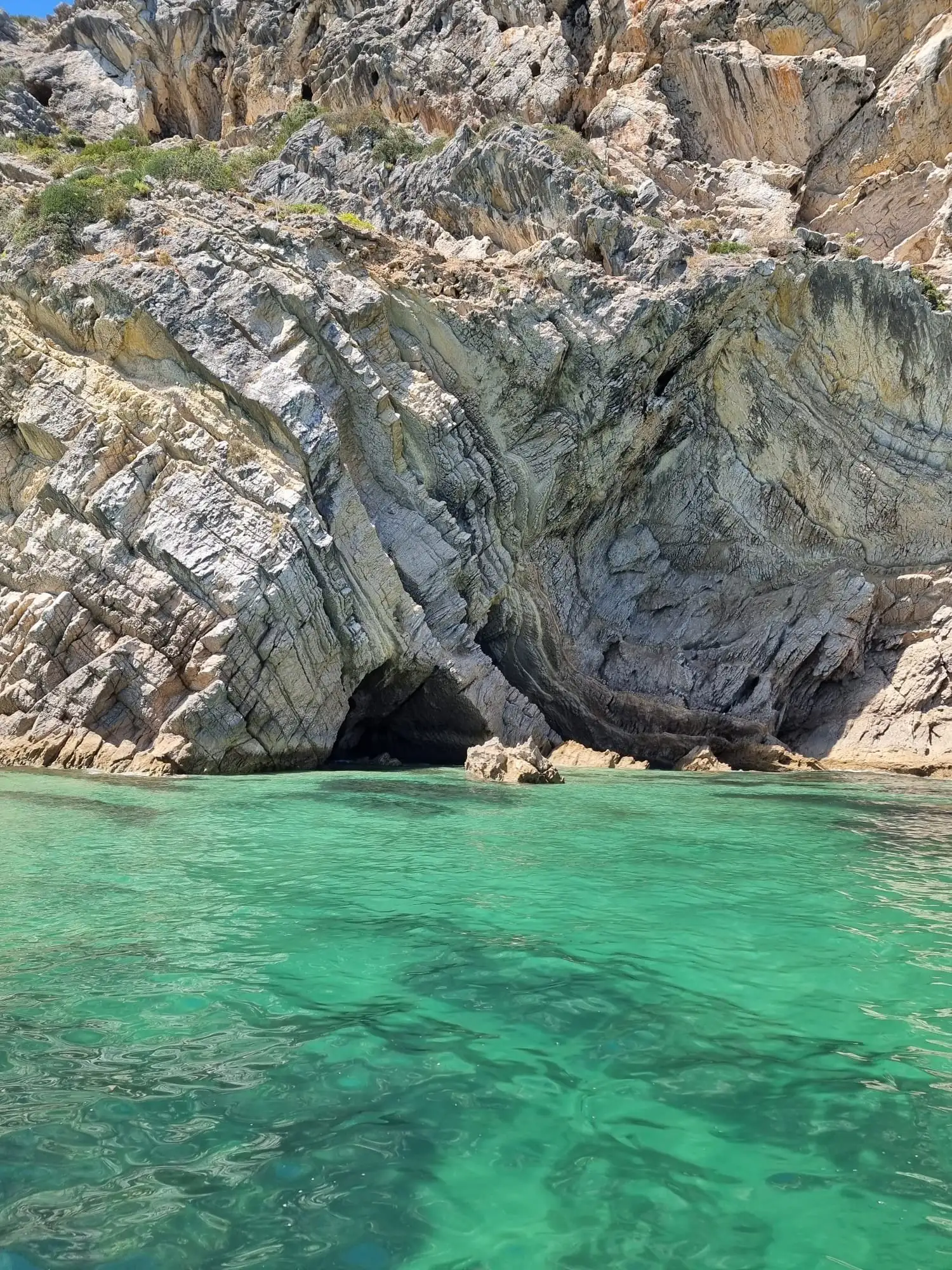 Cave entrance in folded grey rock above clear shallow water