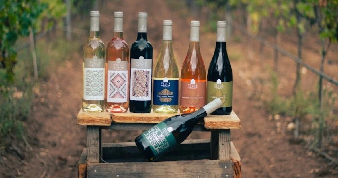 Six bottles of wine on a wooden crate between vineyard rows