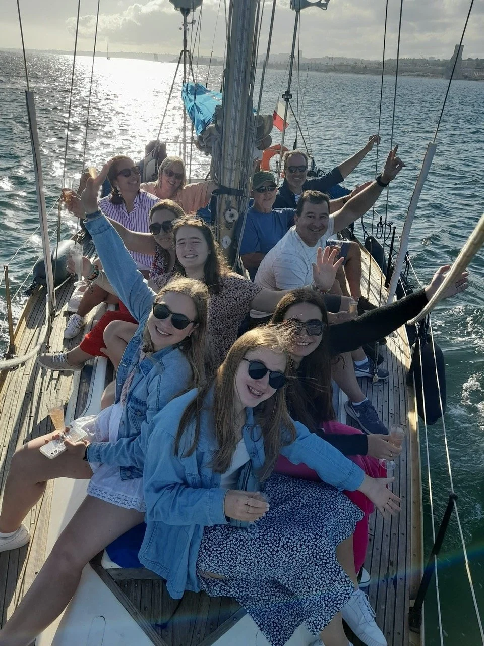 Group of cheering friends sitting along the deck of a sailing boat