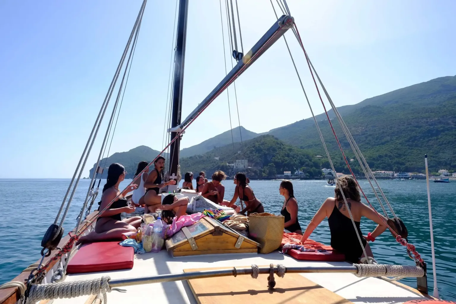 Guests relaxing on the deck of a traditional wooden sailing boat with hills behind