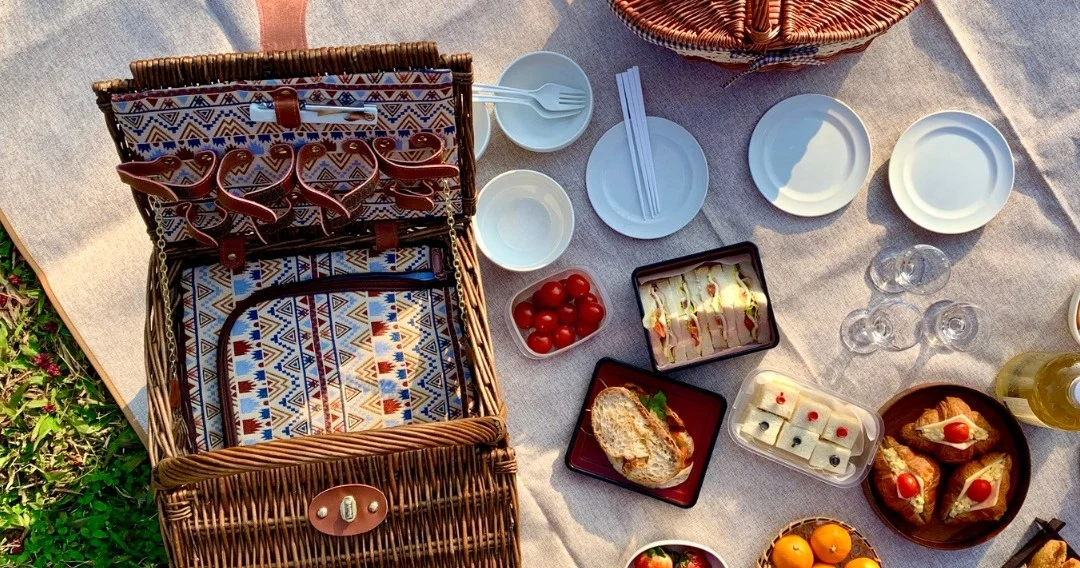 Open picnic basket with plates and snacks on a blanket on the grass