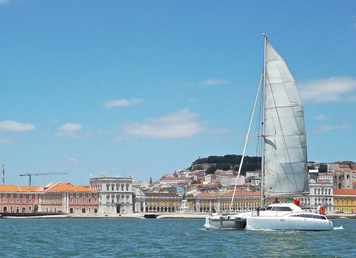 Catamaran sailing in front of a waterfront square and hillside city