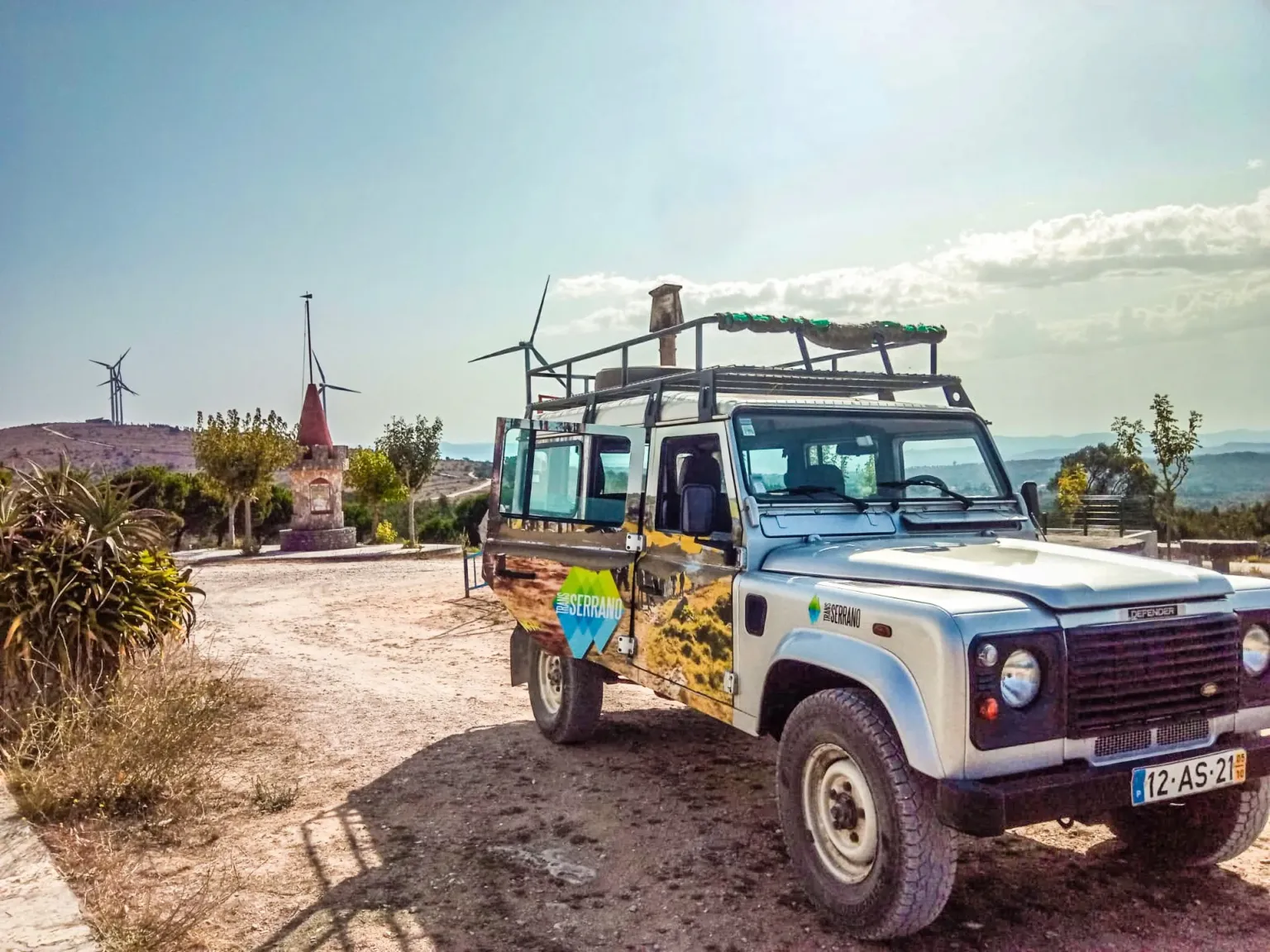 Decorated 4x4 parked beside a viewpoint with wind turbines on the horizon