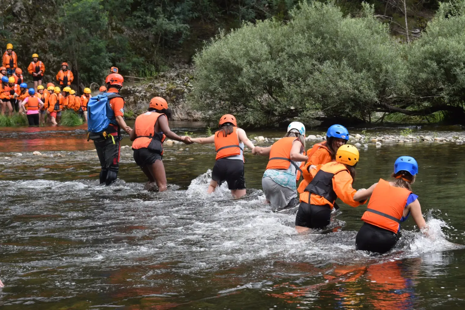 Groep met helmen en zwemvesten waadt door een rivier
