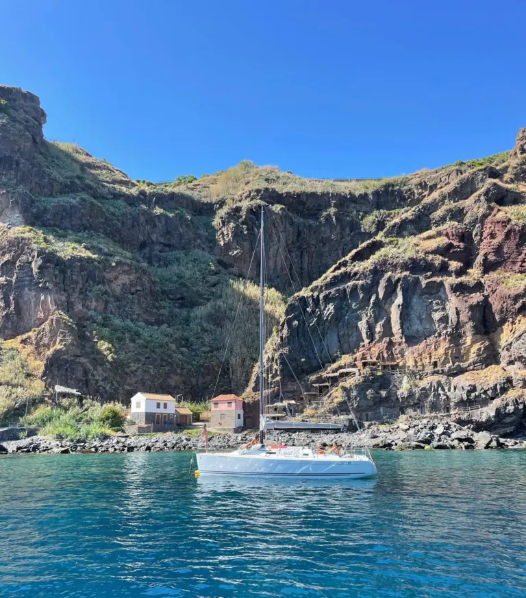 Sailboat anchored in a cove beneath towering volcanic cliffs