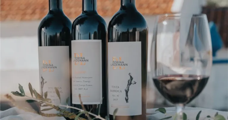 Three bottles of red wine beside a full glass and olive leaves