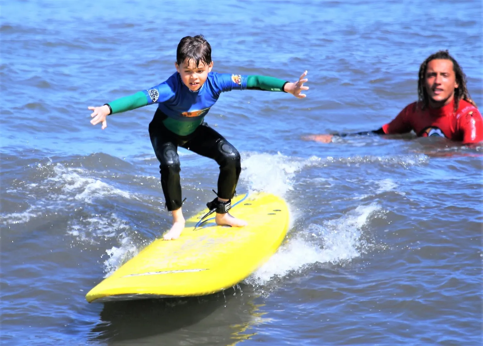 Child in a rash vest standing on a yellow board on a wave