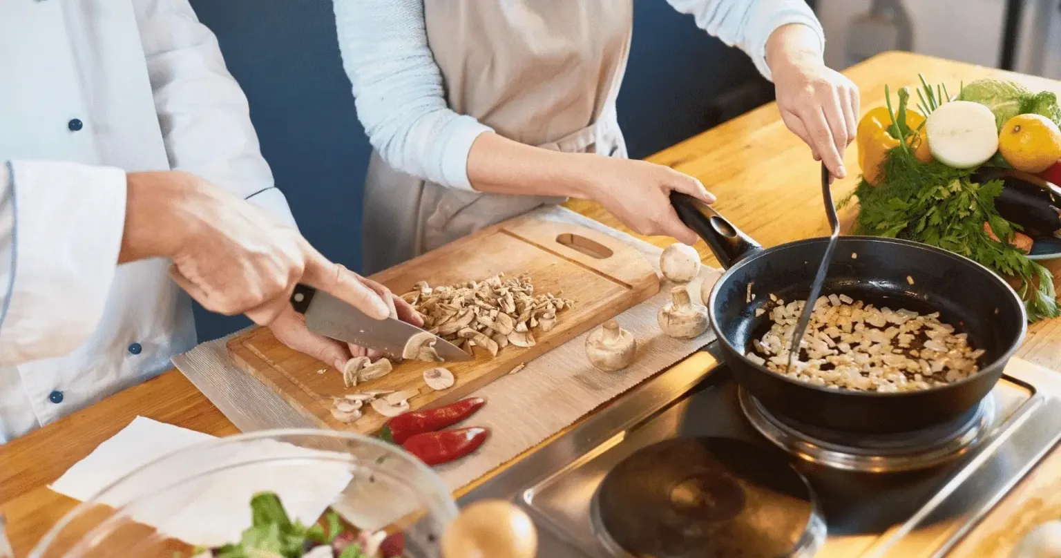 Hands chopping and sautéing ingredients in a pan at a cooking class