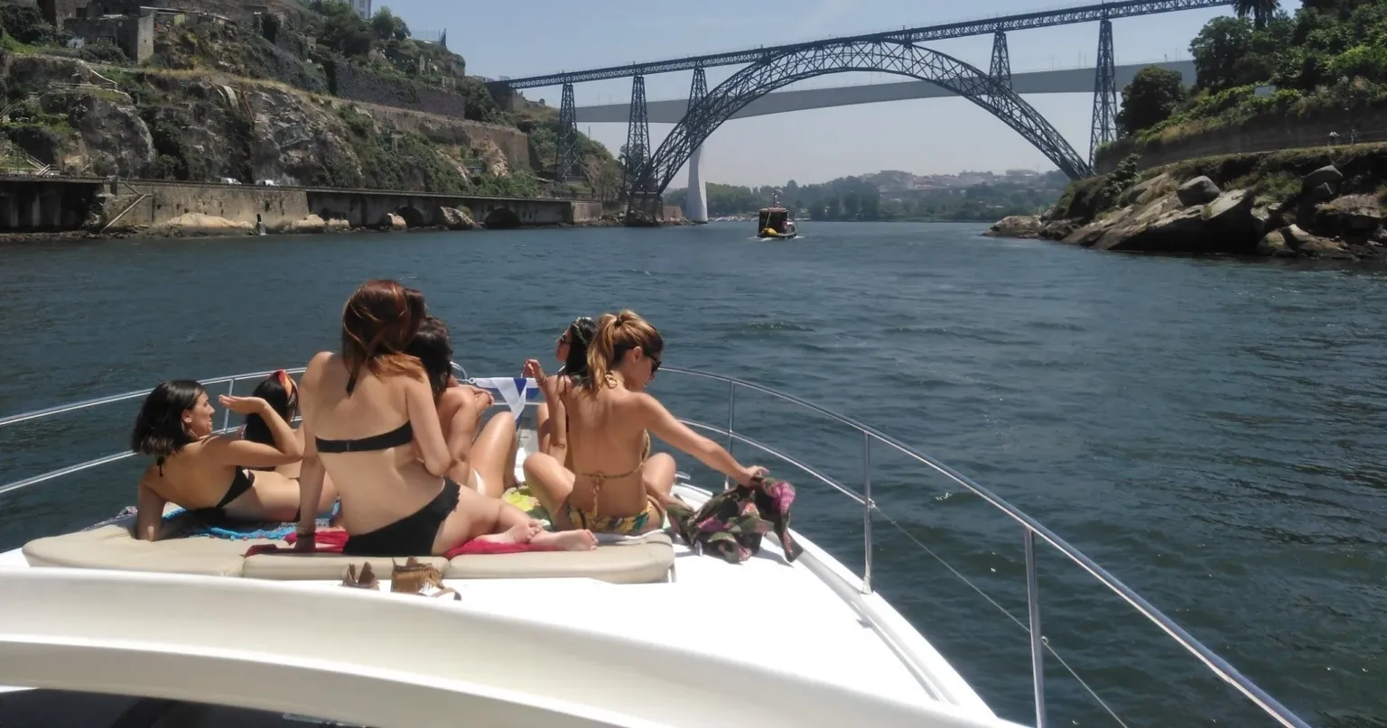 Women sunbathing on the bow of a yacht beneath an iron arch bridge
