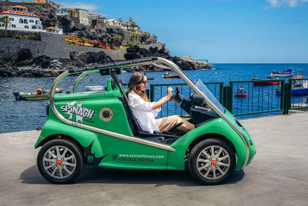 Woman driving a green open buggy along a seafront quay