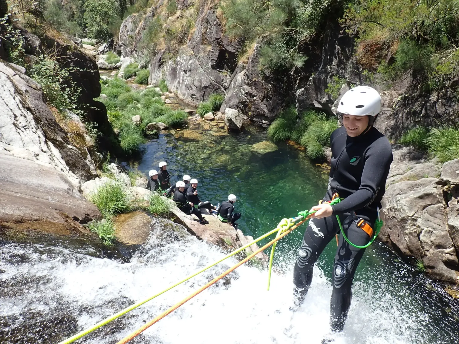 Canyoner abseiling down a waterfall with a group behind