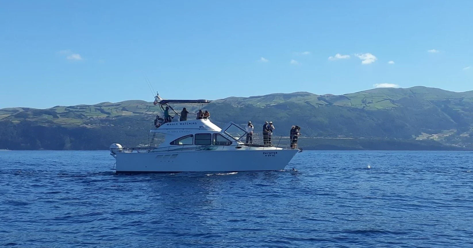 Motor yacht with people on deck at sea, with an island on the horizon