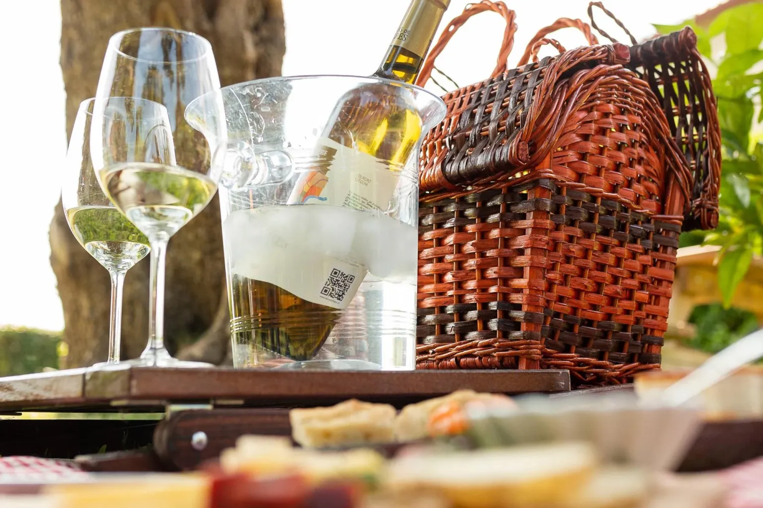 Glasses of white wine, a picnic basket and snacks on a table outdoors